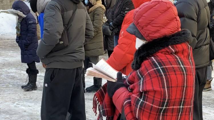 A worshipper wearing a red coat reads a song book in the parking lot of the Montreal Cathedral