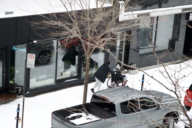 A woman pushes her husband in a wheelchair through the snowy sidewalks of downtown Montreal